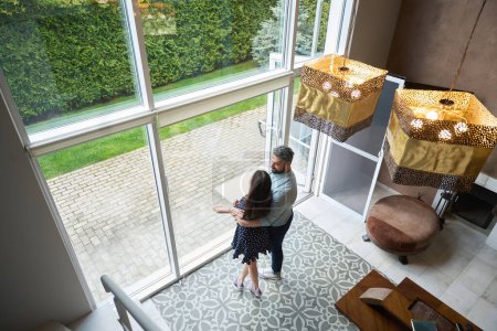 Photo for Happy husband and wife are dancing, hugging each other in spacious living room, outside the window is a cute backyard - Royalty Free Image