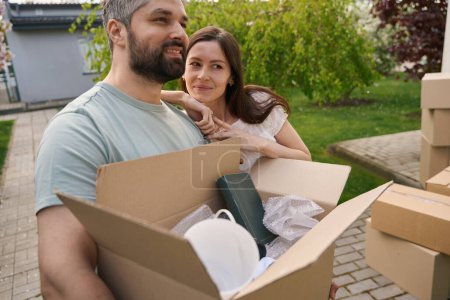 Photo for Attractive woman putting her head on shoulder of her man who carrying heavy box outside - Royalty Free Image