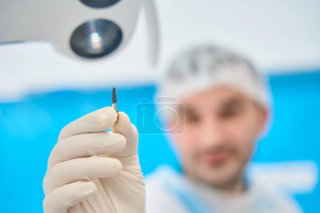 Téléchargez les photos : Dentiste tient dans sa main une broche dentaire pour les prothèses de la dentition - en image libre de droit