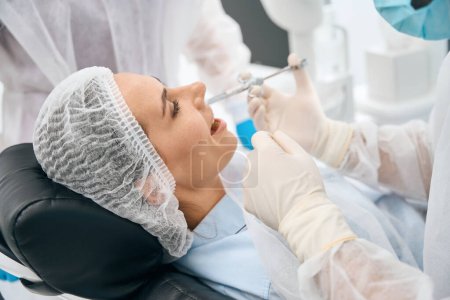 Foto de Mujer en el consultorio dental recibe una inyección de analgésico, el médico trabaja en guantes de protección - Imagen libre de derechos