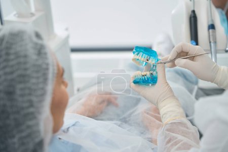 Kieferorthopäde zeigt einem Patienten ein Modell mit Zahnimplantaten, einem Arzt in Schutzhandschuhen