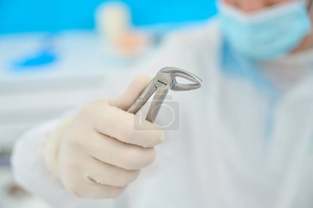 Photo for Doctor holds in his hand a special tool for removing teeth, forceps are made of medical steel - Royalty Free Image