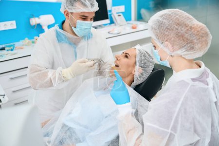 Téléchargez les photos : Dentiste et assistante sur le lieu de travail, le patient dans la chaise dentaire se prépare à l'extraction dentaire - en image libre de droit