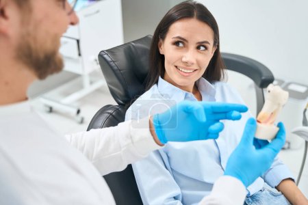 Téléchargez les photos : Femme attrayante regardant le dentiste en toute confiance, écoutant comment il traitera les canaux racinaires dans ses dents, aide spécialisée qualifiée - en image libre de droit
