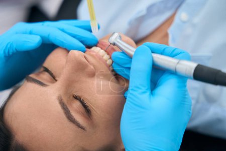 Photo for Close-up nurse holding saliva ejector while dentist in protective gloves holding drill to remove tooth decay before filling a cavity and clean roots - Royalty Free Image
