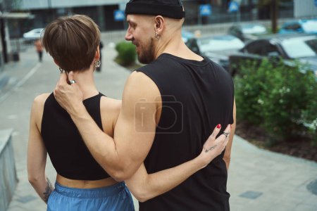 Téléchargez les photos : Les jeunes hommes sont debout, embrassant dans le paysage urbain, ils portent des vêtements de jeunesse confortables - en image libre de droit