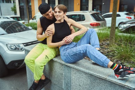 Téléchargez les photos : Jeune couple communique cutely sur un parapet haut sous un arbre, le gars étreint doucement sa petite amie - en image libre de droit