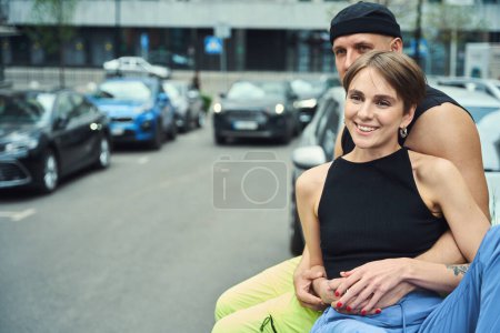 Téléchargez les photos : Jeune couple heureux se détendre sur une promenade en ville, les jeunes en vêtements décontractés, parking à proximité - en image libre de droit