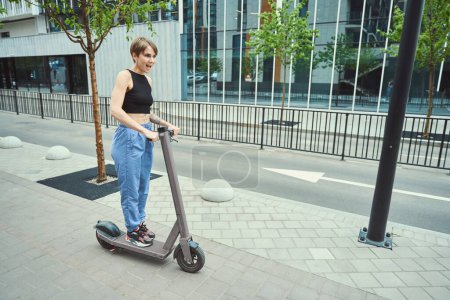 Photo for Female in sportswear rides a scooter through the city streets, she is slim and has a short haircut - Royalty Free Image