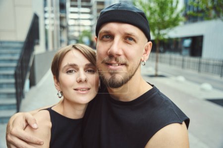 Foto de El tipo barbudo y su novia están de pie, abrazándose unos a otros, en una calle de la ciudad, que están en ropa casual cómoda - Imagen libre de derechos
