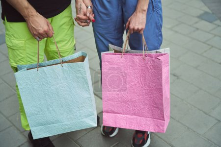 Foto de Guy y una joven hembra de pie tomados de la mano en una calle de la ciudad, tienen bolsas de compras - Imagen libre de derechos
