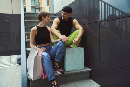 Foto de Joven hombre y mujer están descansando en las escaleras de la ciudad, paquetes con compras están cerca - Imagen libre de derechos