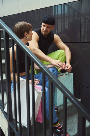 Téléchargez les photos : Homme et sa petite amie se reposent sur les marches des escaliers de la ville, sacs à provisions sont à proximité - en image libre de droit