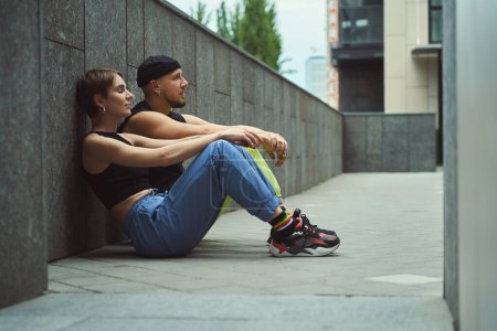 Téléchargez les photos : Jeune femme et son amie bavardent assis sur le trottoir dans une petite cour d'une métropole - en image libre de droit