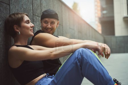 Téléchargez les photos : Jeune homme informel et sa petite amie bavardent assis sur le trottoir dans une petite cour dans une métropole - en image libre de droit