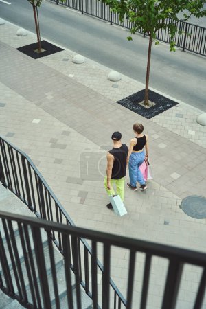 Photo for Young woman and a man walk along the sidewalk, holding hands, they have shopping bags - Royalty Free Image