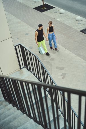 Foto de Guy y su novia están caminando por la acera, tomados de la mano, chicos en un paseo por la ciudad - Imagen libre de derechos