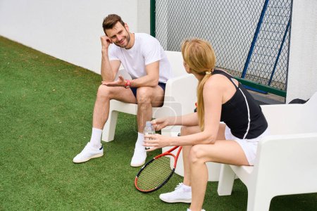 Photo for Couple communicate while sitting in chairs on the tennis court, the woman drinks clean water - Royalty Free Image