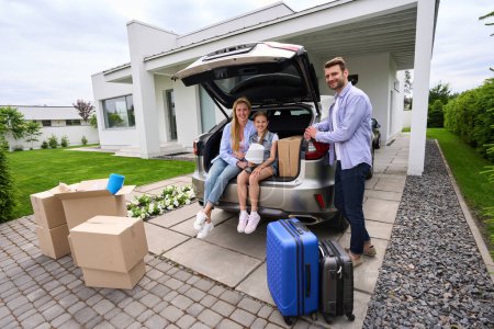 Téléchargez les photos : Bonne famille déménage dans une nouvelle maison moderne, voitures et boîtes en carton sont sur le site - en image libre de droit