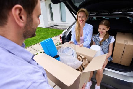 Photo for Mom, dad and daughter move to a new modern house, a man carries a box with things - Royalty Free Image
