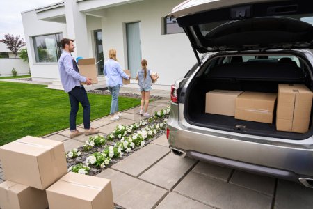 Téléchargez les photos : Les gens portent des boîtes en carton avec des choses de la voiture à une nouvelle maison, la famille se déplace - en image libre de droit
