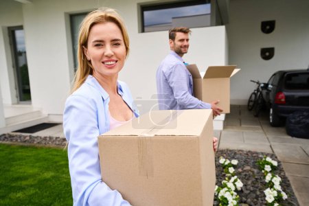 Photo for Wife and husband carry boxes with things to a new house, green lawn in the yard - Royalty Free Image