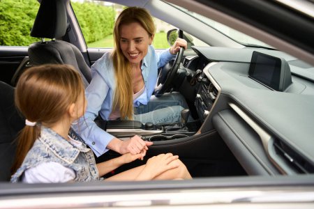 Téléchargez les photos : Maman blonde avec sa fille adolescente sont assis dans la voiture, la femme tient la fille par la main - en image libre de droit