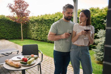 Foto de Esposo y esposa se relajan en el patio trasero de su casa de campo, tienen una copa de vino - Imagen libre de derechos