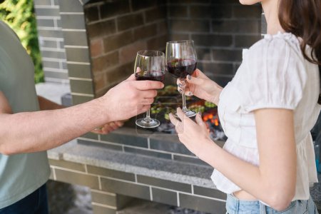 Téléchargez les photos : L'homme et la femme se détendent dans la zone grillagée avec un verre de vin, la nourriture est préparée sur des charbons - en image libre de droit