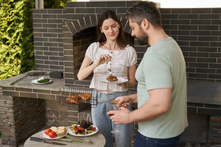 Téléchargez les photos : Mari cuisine de la nourriture et discute avec sa femme dans la cour près du grand four dans la zone de grill - en image libre de droit