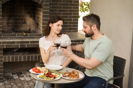Foto de Marido y la esposa de mediana edad cenan en la carne y el vino en el patio trasero, la pareja se encuentra en la zona de la parrilla - Imagen libre de derechos