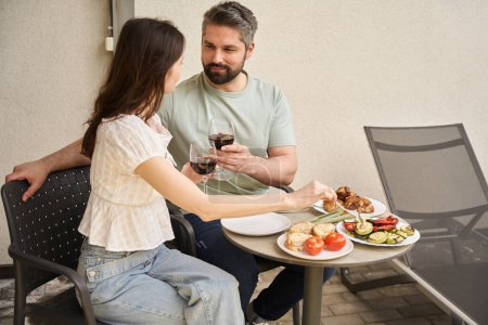 Photo for Middle-aged couple sit down with food and wine at their cottage, they communicate nicely - Royalty Free Image