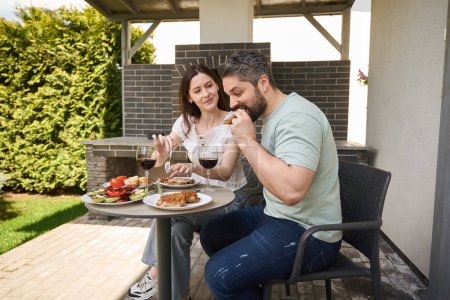 Foto de Hombre y mujer de mediana edad cenan en carne y vino en el patio trasero, la pareja se encuentra en la zona de la parrilla - Imagen libre de derechos
