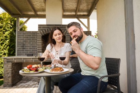 Téléchargez les photos : Femme et mari dînent avec de la viande et du vin dans la cour arrière, le couple est situé dans la zone de grill - en image libre de droit