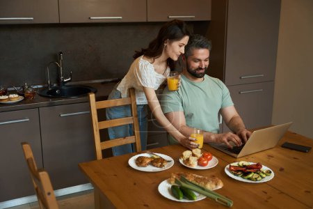 Foto de Esposos de mediana edad se comunican en una acogedora cocina, una mujer trata a un hombre con jugo - Imagen libre de derechos
