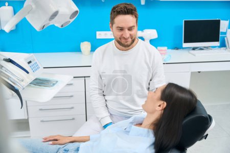 Foto de Mujer visitando el consultorio del dentista, sentada en cómodo sillón y escuchando consejos médicos sonrientes, chequeo de rutina para prevenir problemas dentales - Imagen libre de derechos