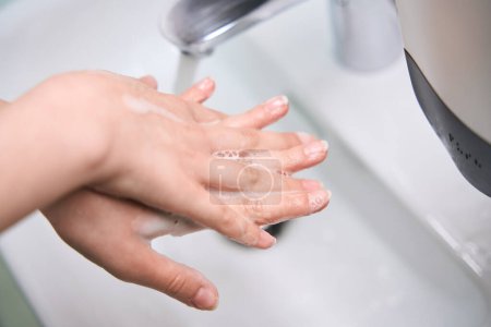 Téléchargez les photos : Femme se lave les mains savonneuses sous le robinet, la patiente a une manucure soignée - en image libre de droit