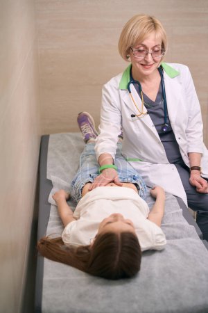 Photo for Pediatrician at the reception probes the girls stomach, the child lies on a medical couch - Royalty Free Image