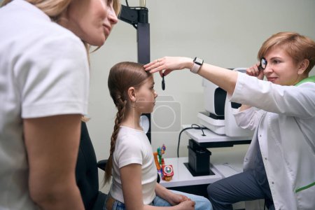 Jeune patient est à la clinique à un rendez-vous avec un ophtalmologiste, à côté de la mère de l'enfant