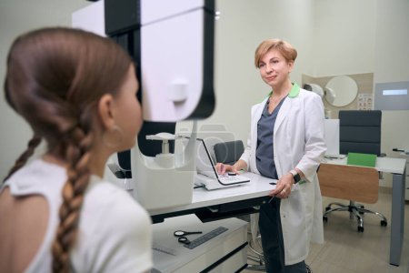 Téléchargez les photos : Ophtalmologiste spécialiste examine les yeux d'une fille sur l'équipement moderne, une femme en robe médicale - en image libre de droit