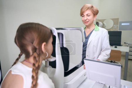 Téléchargez les photos : Ophtalmologiste sur le lieu de travail examine les yeux d'un jeune patient sur un appareil spécial, le médecin utilise un équipement moderne - en image libre de droit