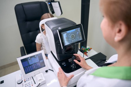 Foto de Oftalmólogo especialista examina los ojos de un paciente joven en un aparato especial, el médico utiliza equipos modernos - Imagen libre de derechos