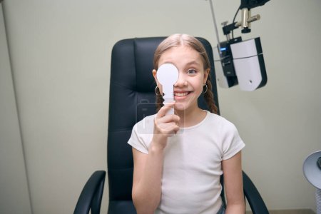 Photo for Young patient in the clinic on an ophthalmological diagnostic test, a girl with two pigtails - Royalty Free Image