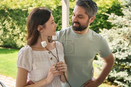 Téléchargez les photos : Heureux couple marié se reposant dans la cour de leur chalet, femme a guimauves sur bâtons - en image libre de droit