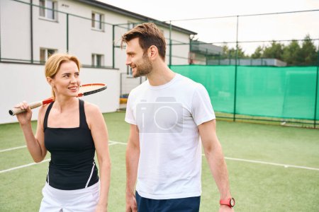 Téléchargez les photos : Femme et homme, parlant, marchant le long du court de tennis, il y a un bâtiment de deux étages à proximité - en image libre de droit