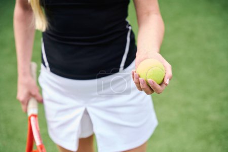 Foto de Raqueta de tenis y pelota amarilla en manos de una joven, hierba verde en la cancha - Imagen libre de derechos