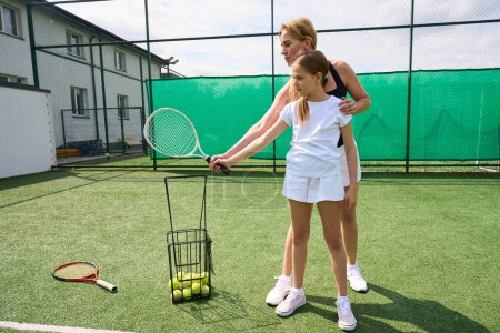 Foto de Mujer joven enseña a una adolescente a jugar al tenis, tienen raquetas de tenis en sus manos - Imagen libre de derechos