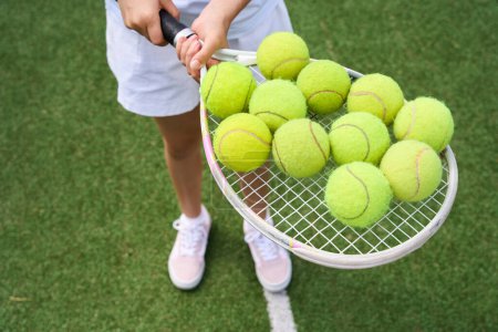 Foto de Chica tiene un montón de bolas amarillas en una raqueta de tenis, hierba verde en la cancha - Imagen libre de derechos