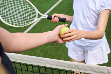 Photo for Young woman passes tennis ball to girl, female and child on tennis court - Royalty Free Image