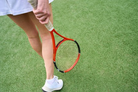 Téléchargez les photos : Femme avec de belles jambes fines marchant le long du court de tennis, elle a une raquette de tennis dans ses mains - en image libre de droit